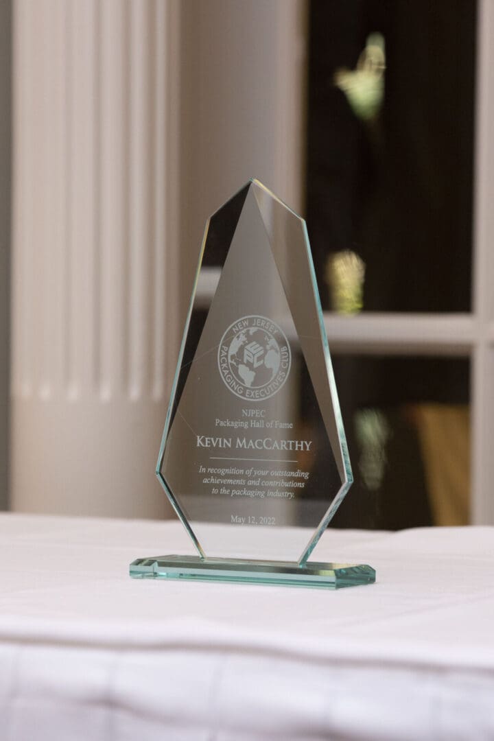 A glass award sits on a table in front of a room.