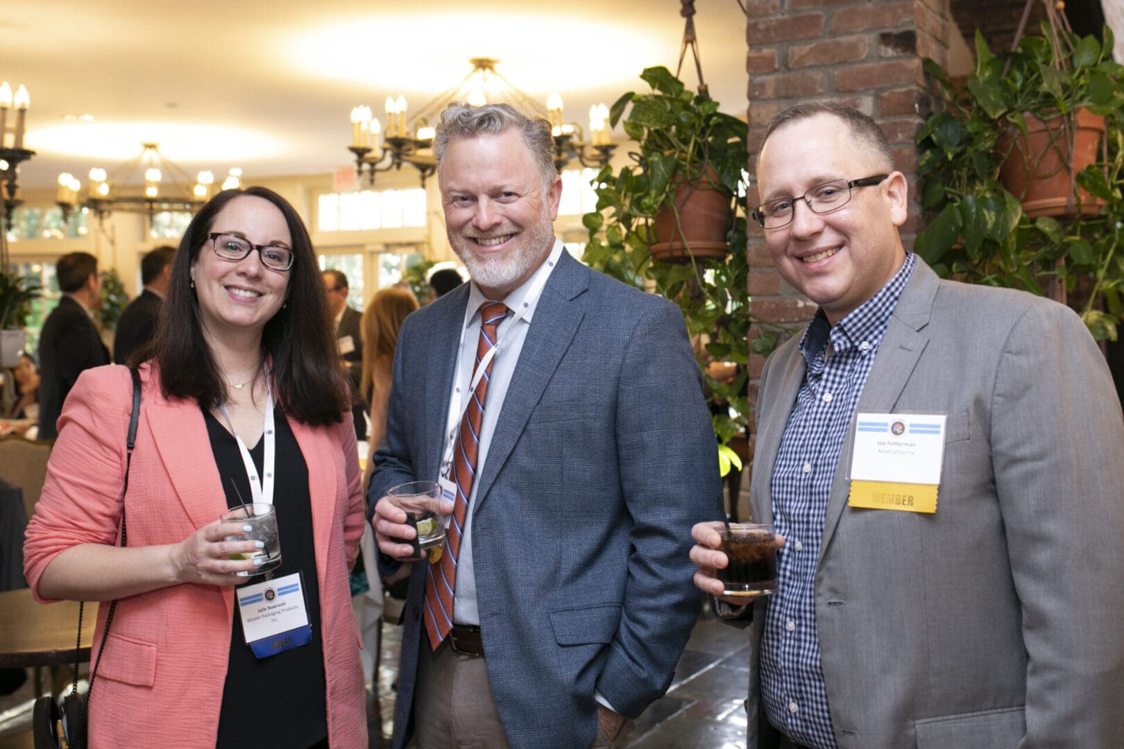 Three people smiling at an event with drinks in their hands.
