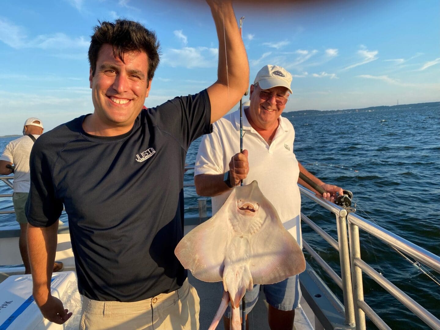 Two men on a boat holding up a stingray.