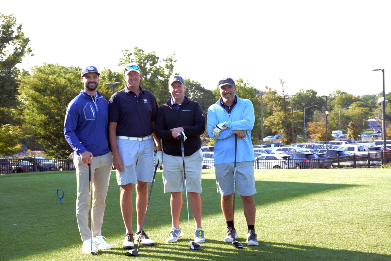 four smiling men wearing caps and holding golf clubs