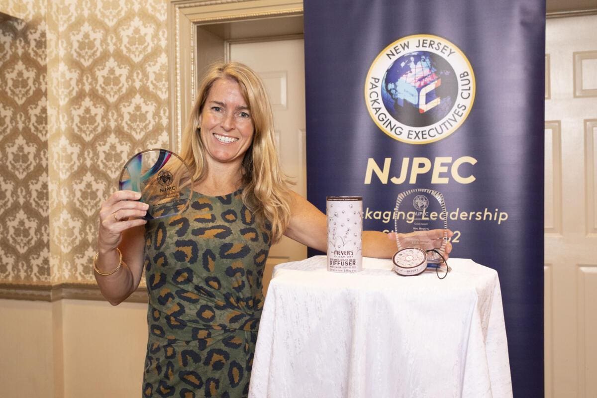 smiling blonde woman in leopard print dress holding award beside white table