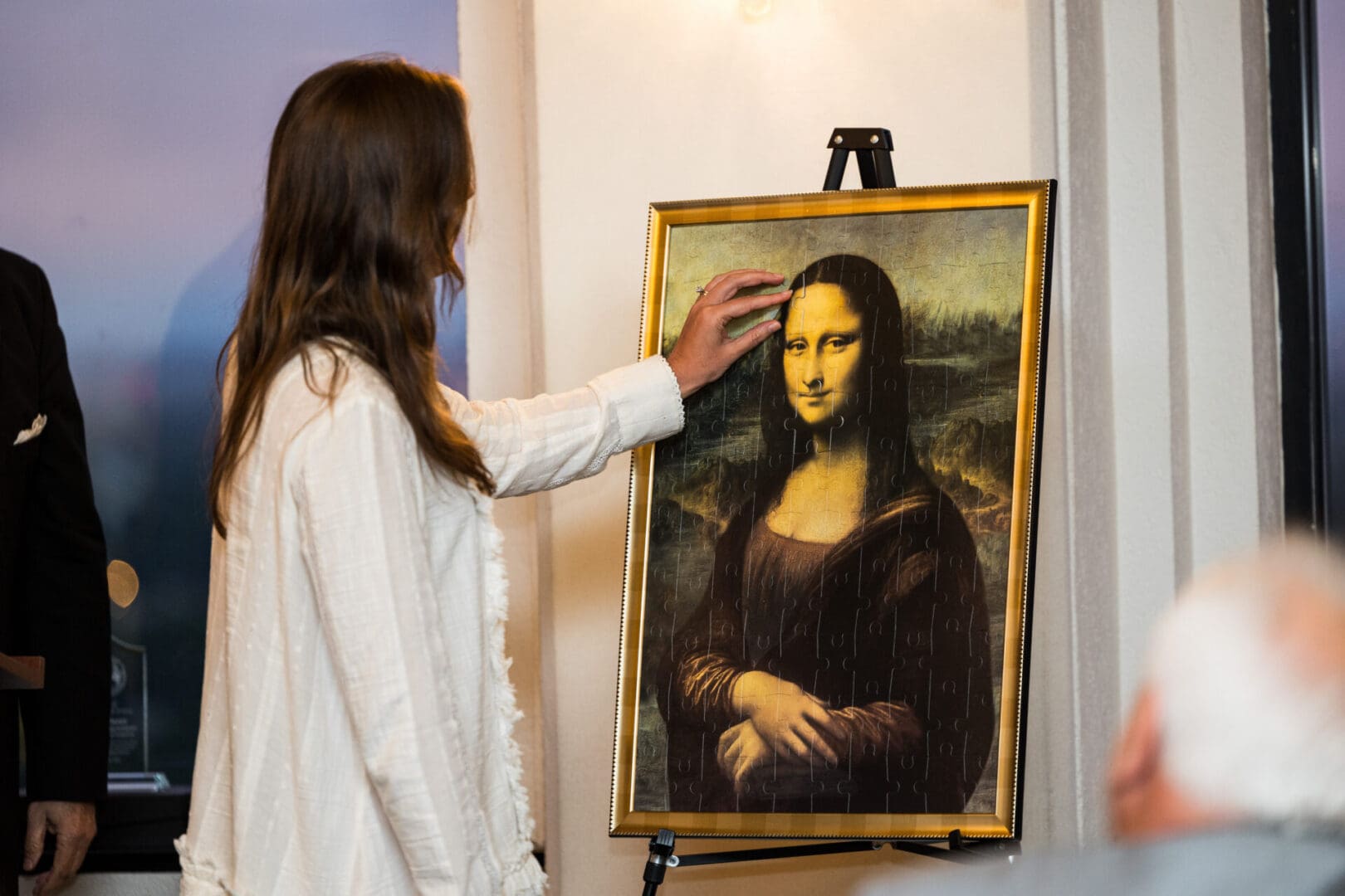 Woman completing Mona Lisa puzzle with one hand.