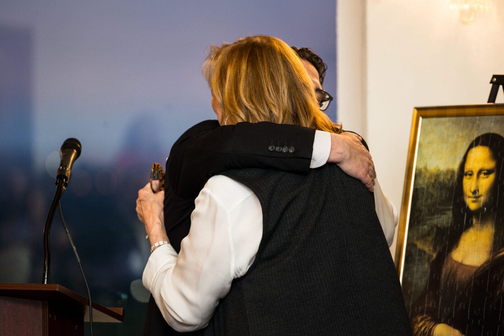 Two people hugging in front of a painting.