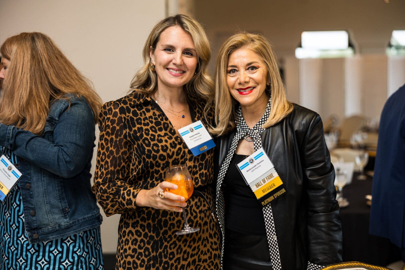 Two women in business attire smiling at a networking event.