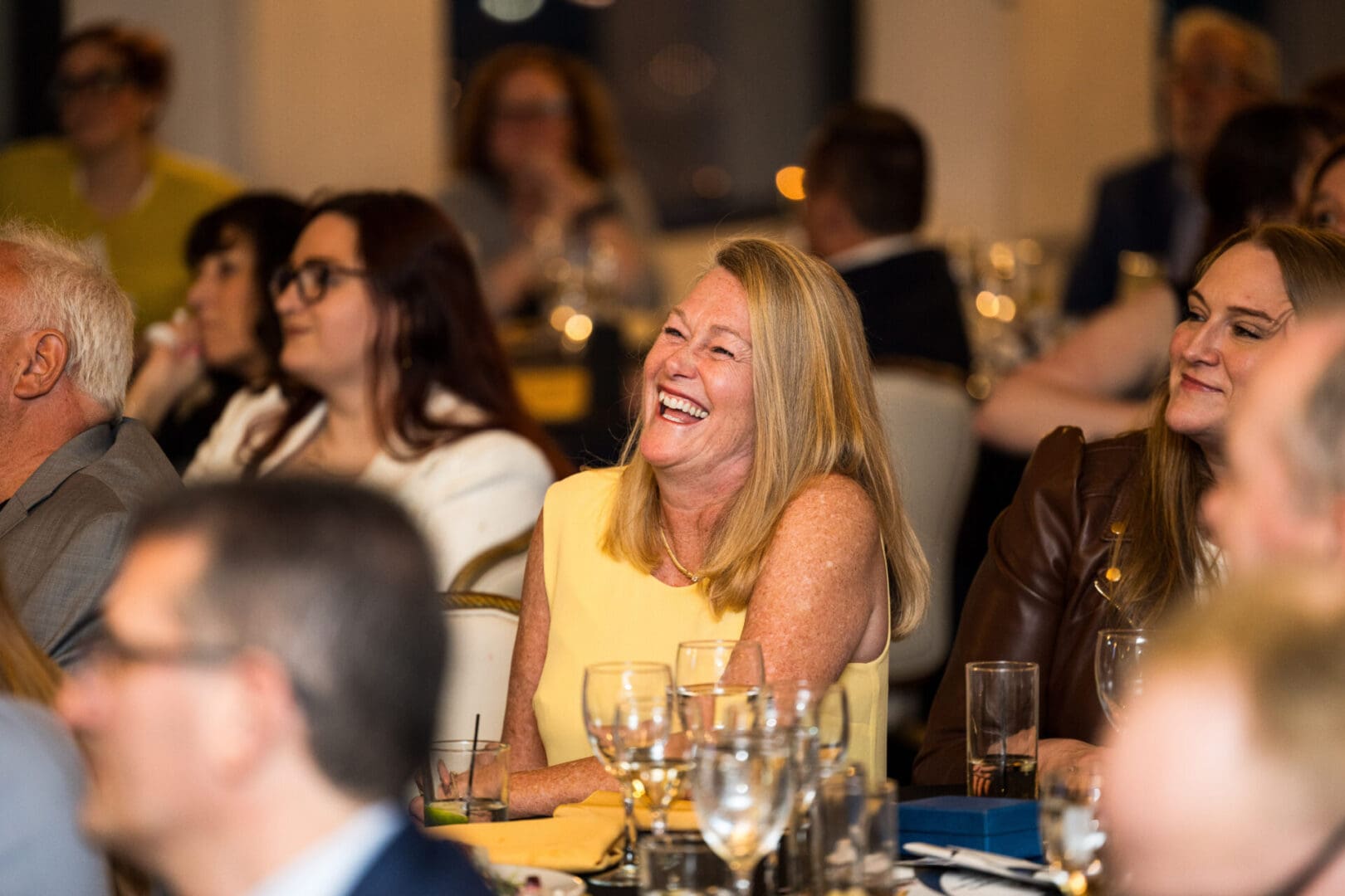 A blonde woman laughs at a dinner party.