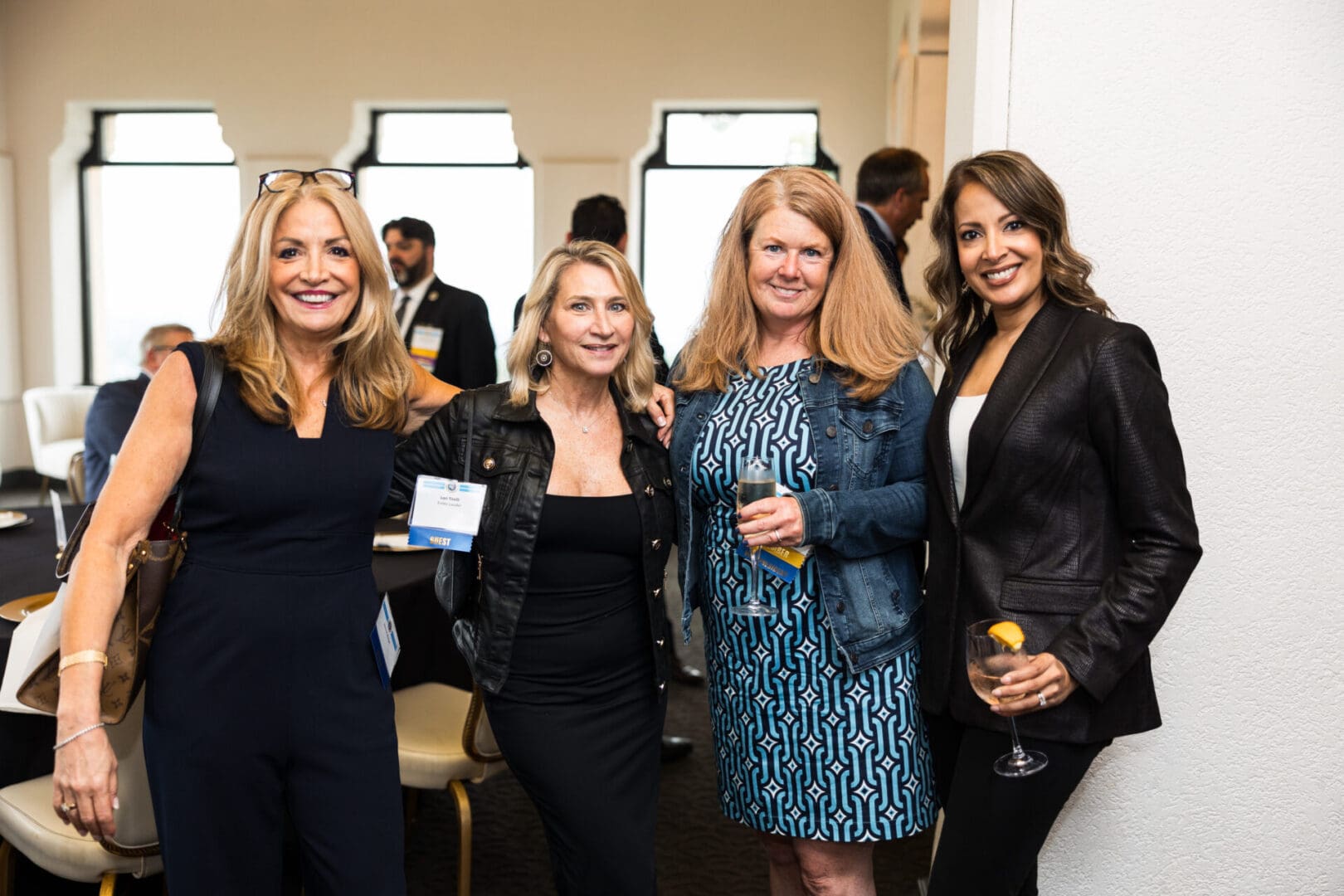 Four smiling women in business attire at an event.