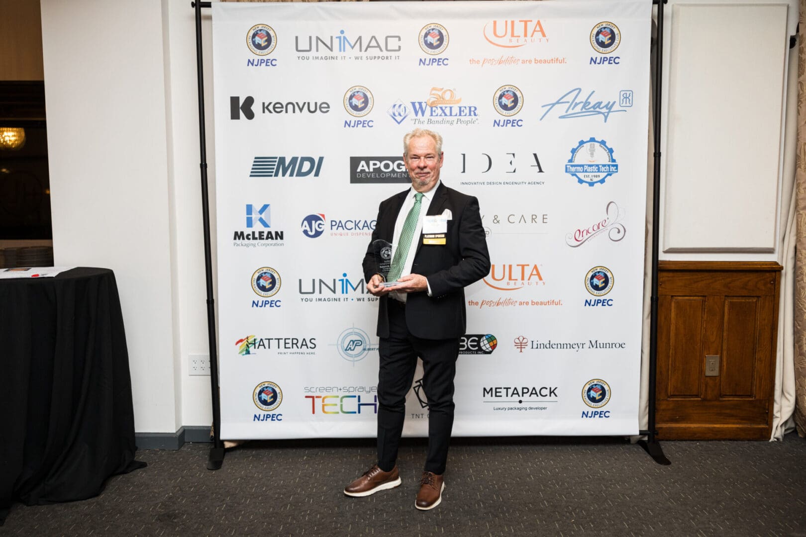 Man in suit holding an award in front of a logo wall.